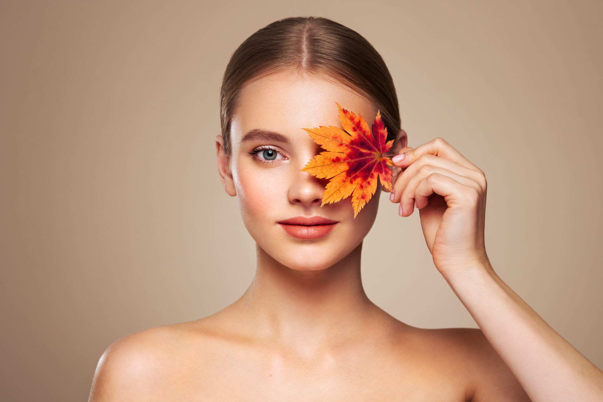 Mujer con una hoja de otoño junto al rostro